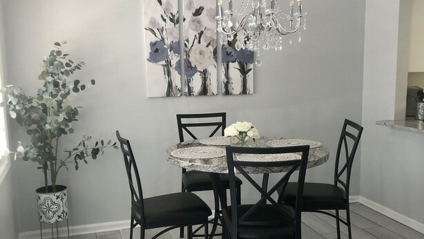 Een eetruimte met een ronde tafel, zwarte stoelen, een kroonluchter en een bloemschilderij aan de muur.