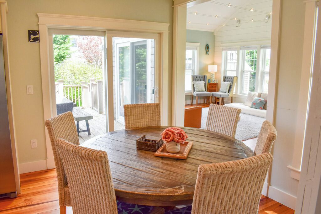 A round wooden table with wicker chairs, a vase of flowers, and a small basket.