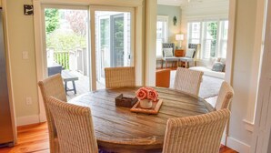 A round wooden table with wicker chairs, a vase of flowers, and a small basket. - Beautiful and pristine 4 bedroom home,  7 minute walk to the Beach! (West Yarmouth)