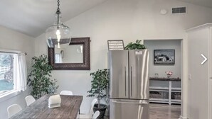 Een moderne keuken met een houten eettafel, witte stoelen, een roestvrijstalen koelkast en een hangende pendantlamp.