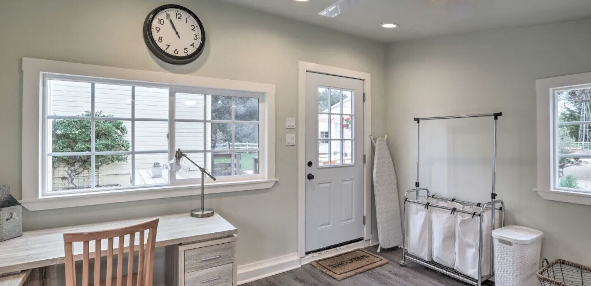 A bathroom with a large window, a door, a towel rack, a sink, and a clock.