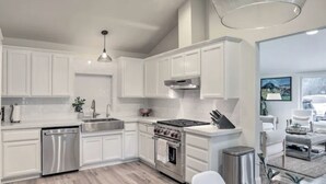 Een moderne keuken met witte kastjes, roestvrijstalen apparatuur en een eethoek met wit meubilair.