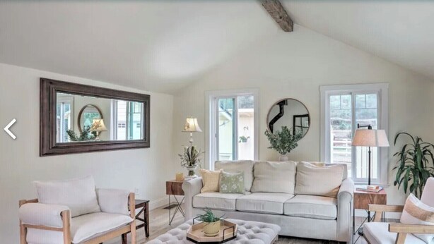 Een ruime woonkamer met een groot raam, een bank, twee fauteuils, een salontafel en een open haard.