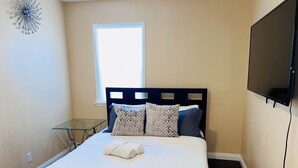 A neatly made bed with patterned pillows, a glass side table, and a TV mounted on the wall. - Cozy Home of Arcadia Central (Arcadia)