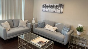 A living room with two grey sofas, a glass coffee table, and a painting of palm trees. - Cozy Home of Arcadia Central (Arcadia)