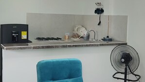 Un salón moderno con un sillón azul, un sofá blanco y una zona de cocina con estufa a gas y ventilador.