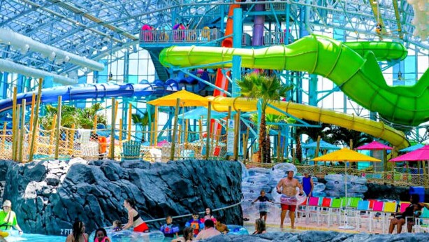 Um parque aquático coberto com teto de vidro amplo, várias escorregas aquáticas e área de piscina.