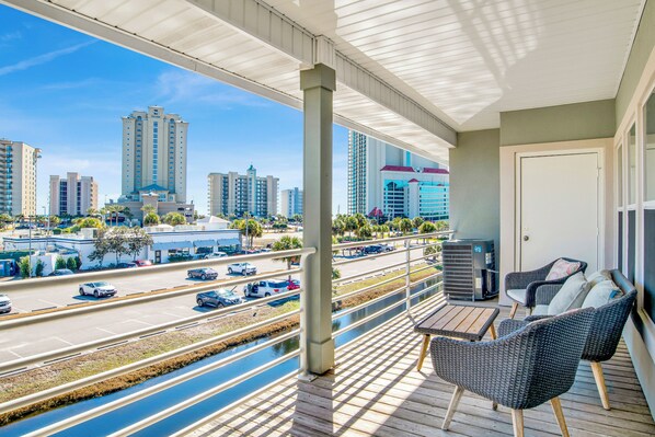 A balcony with wicker chairs and a table, overlooking a cityscape with tall buildings and a highway.