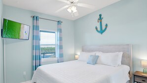 Quarto com cama, ventilador de teto, televisão na parede e janela com cortinas.