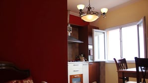 A compact kitchen with a dining area, a window providing natural light, and a red wall.
