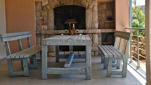 An outdoor seating area with a stone fireplace, wooden benches, and a table with a bottle and glass.
