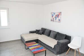 A modern living room with a grey sectional sofa, a colorful striped bench, and a white chair.