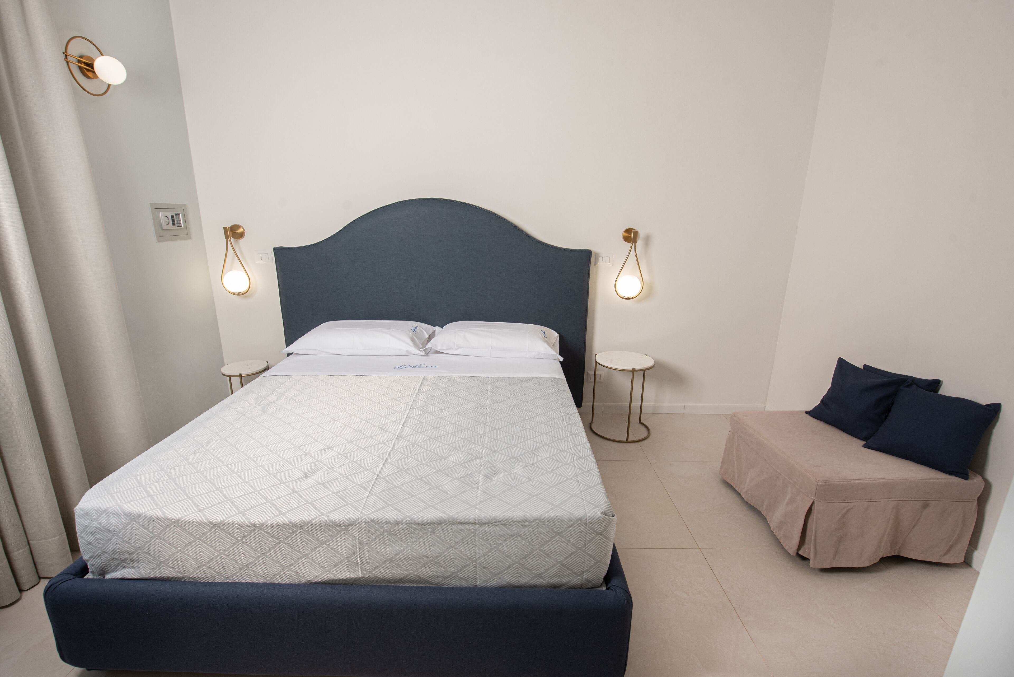 A neatly arranged bedroom with a bed, bedside tables, and a sofa.