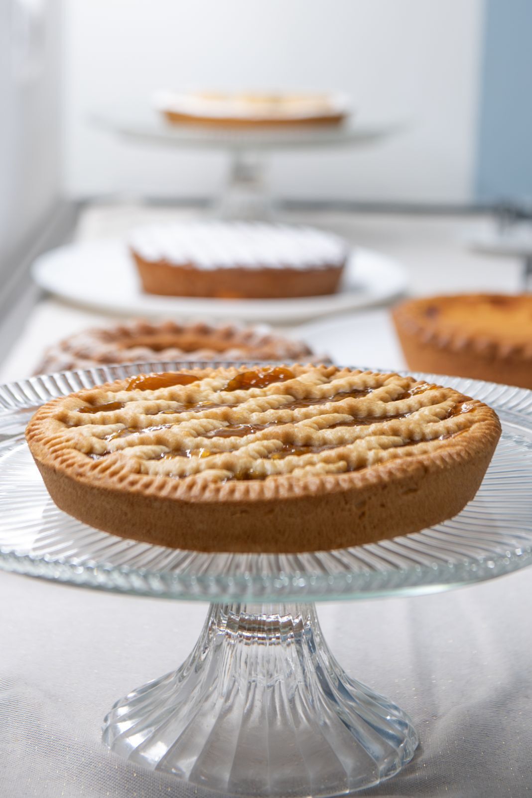 A pie on a glass stand with a blurred background of other pies.