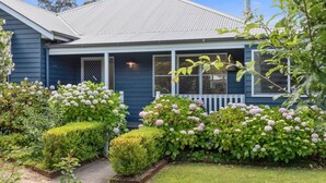A house with a blue exterior, a front porch, and a well-maintained garden with hydrangeas.