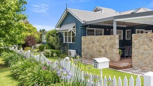 A house with a stone wall entrance, a covered porch, and a well-maintained garden with a white picket fence.