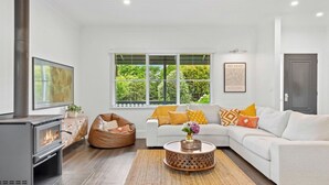 A modern living room with a fireplace, a white sofa, a bean bag, and a large window with a view of greenery.