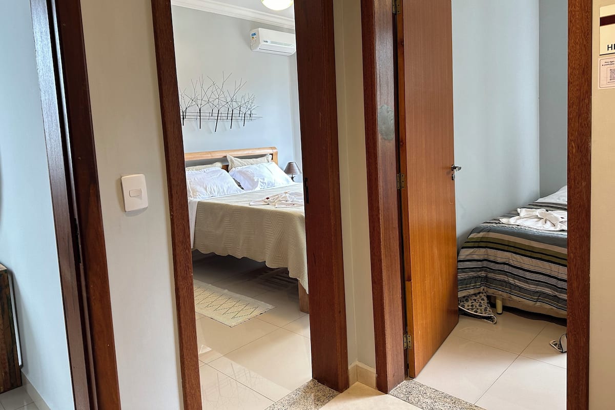 Quarto de hotel com uma cama, mesa de cabeceira e ar condicionado fixado na parede.