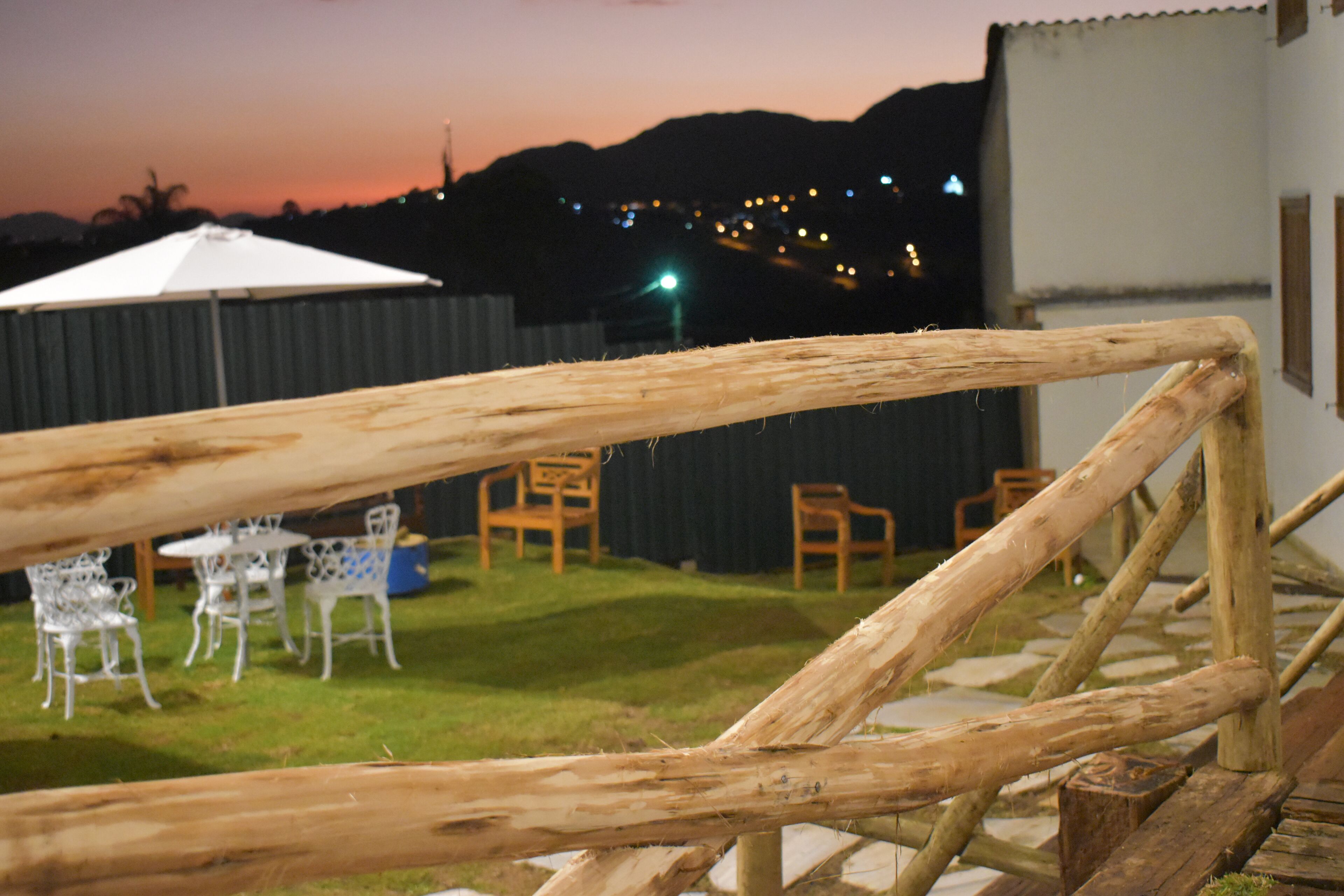 Una cerca de madera en un patio trasero con mobiliario exterior y vistas a un paisaje urbano al anochecer.