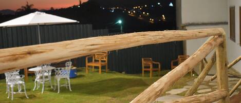 Una cerca de madera en un patio trasero con mobiliario exterior y vistas a un paisaje urbano al anochecer.