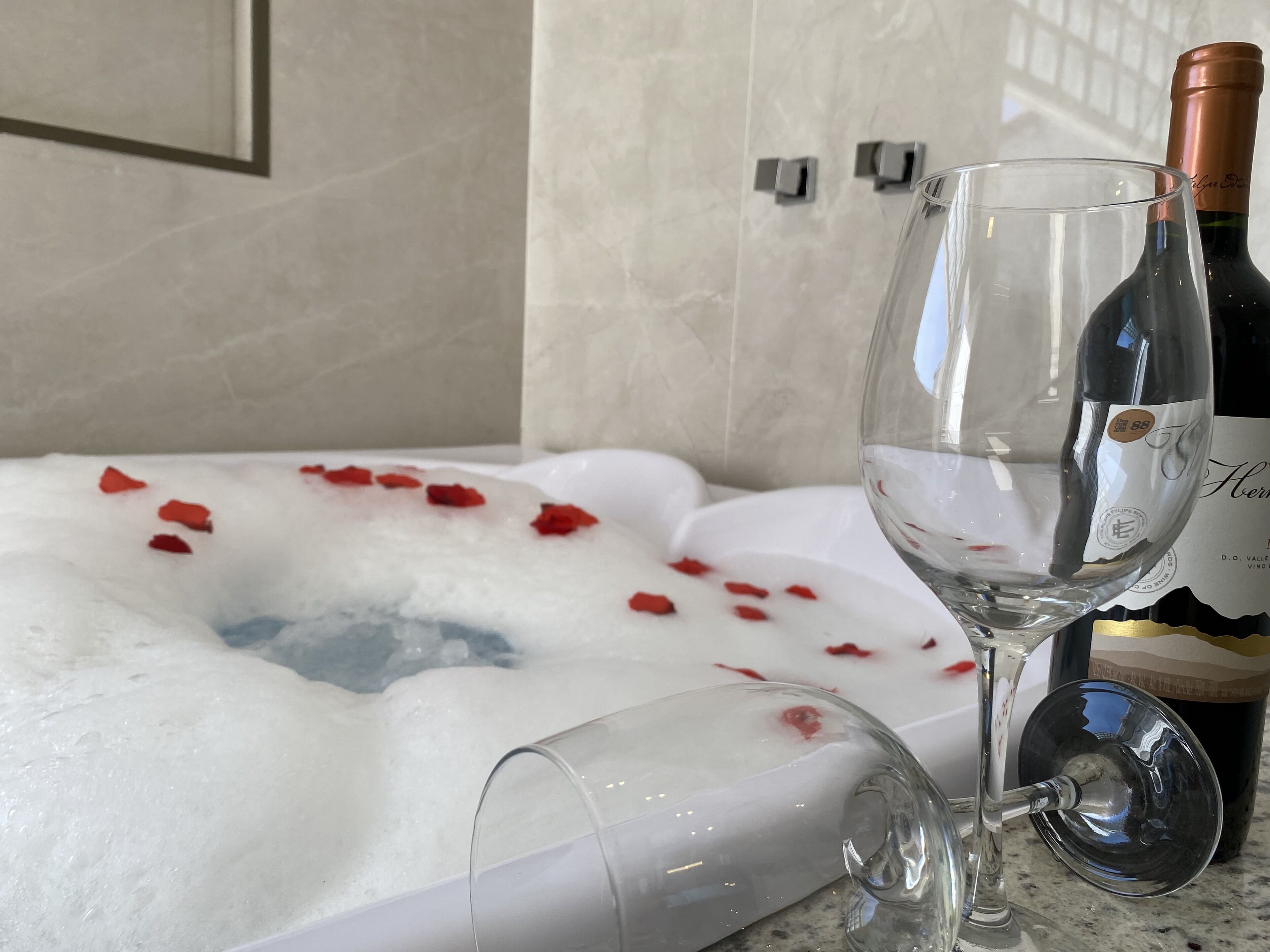 Un bain à remous rempli de pétales de rose, une bouteille de vin et un verre à vin.