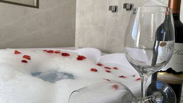 Un bain à remous rempli de pétales de rose, une bouteille de vin et un verre à vin.