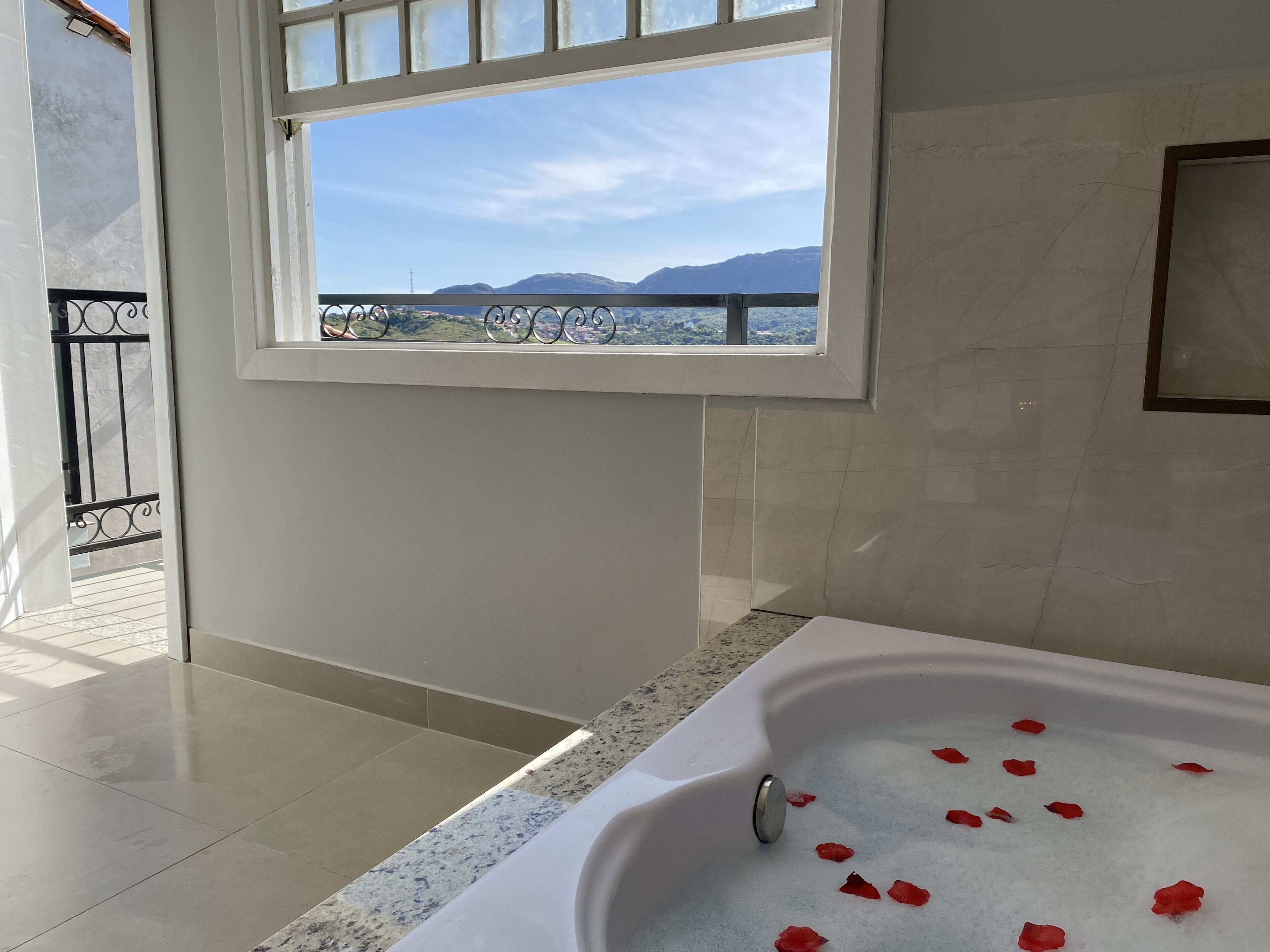 Un baño con bañera, ventana con vistas a montañas y balcón con barandilla.