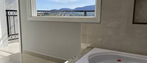Un baño con bañera, ventana con vistas a montañas y balcón con barandilla.