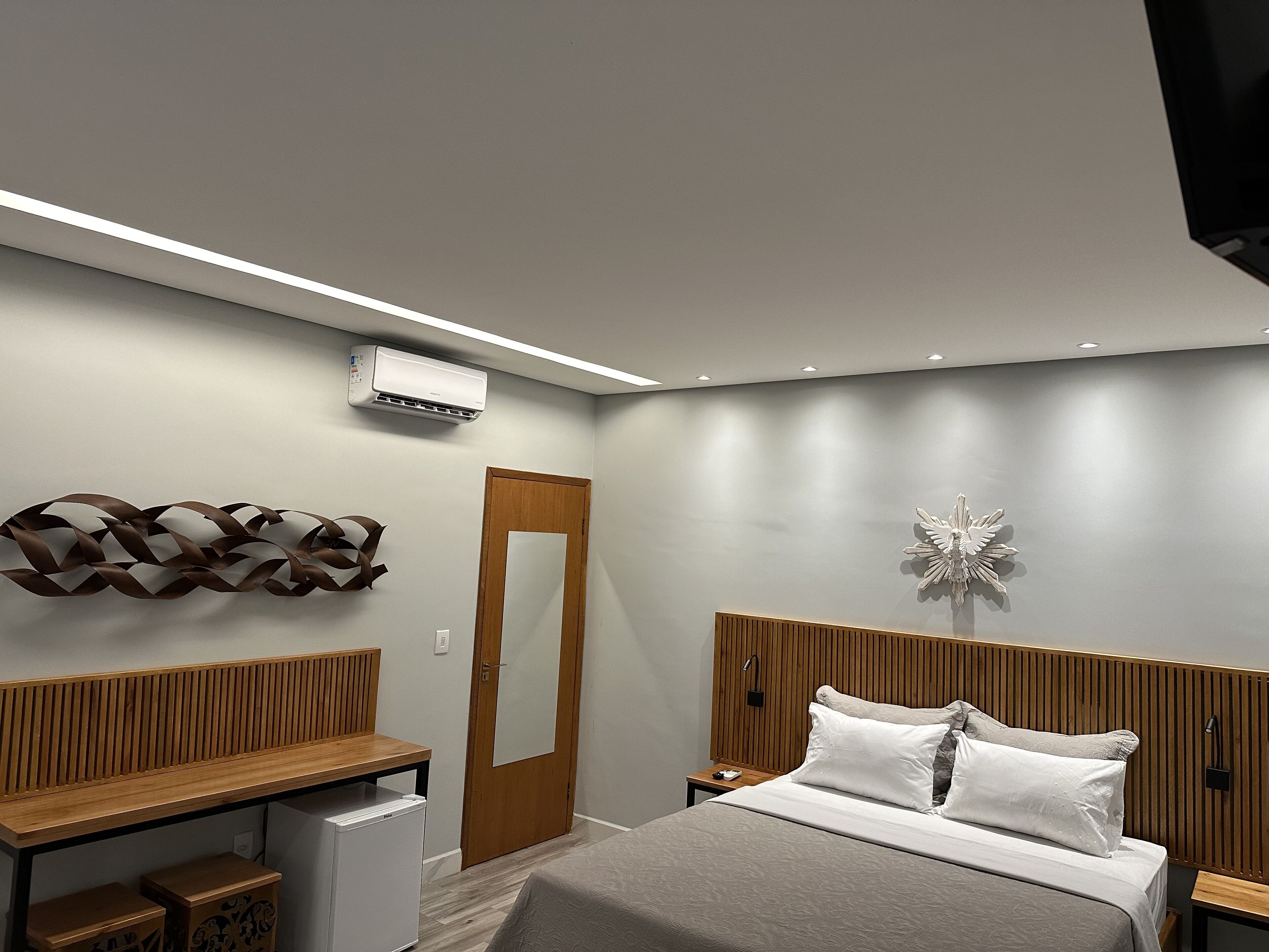A modern bedroom with a bed, bedside tables, a wooden headboard, a wall-mounted air conditioner, and a decorative wall piece.