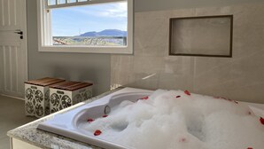 Un baño con una bañera llena de burbujas, una ventana con vistas a montañas y una puerta.