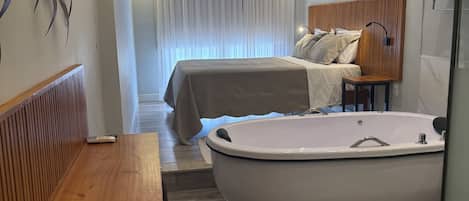 A modern bedroom with a large bathtub, a wooden bench, and a bed with a headboard.