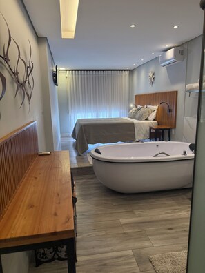 A modern bedroom with a large bathtub, a wooden bench, and a bed with a headboard. - Pousada Maria Monteiro (Tiradentes)
