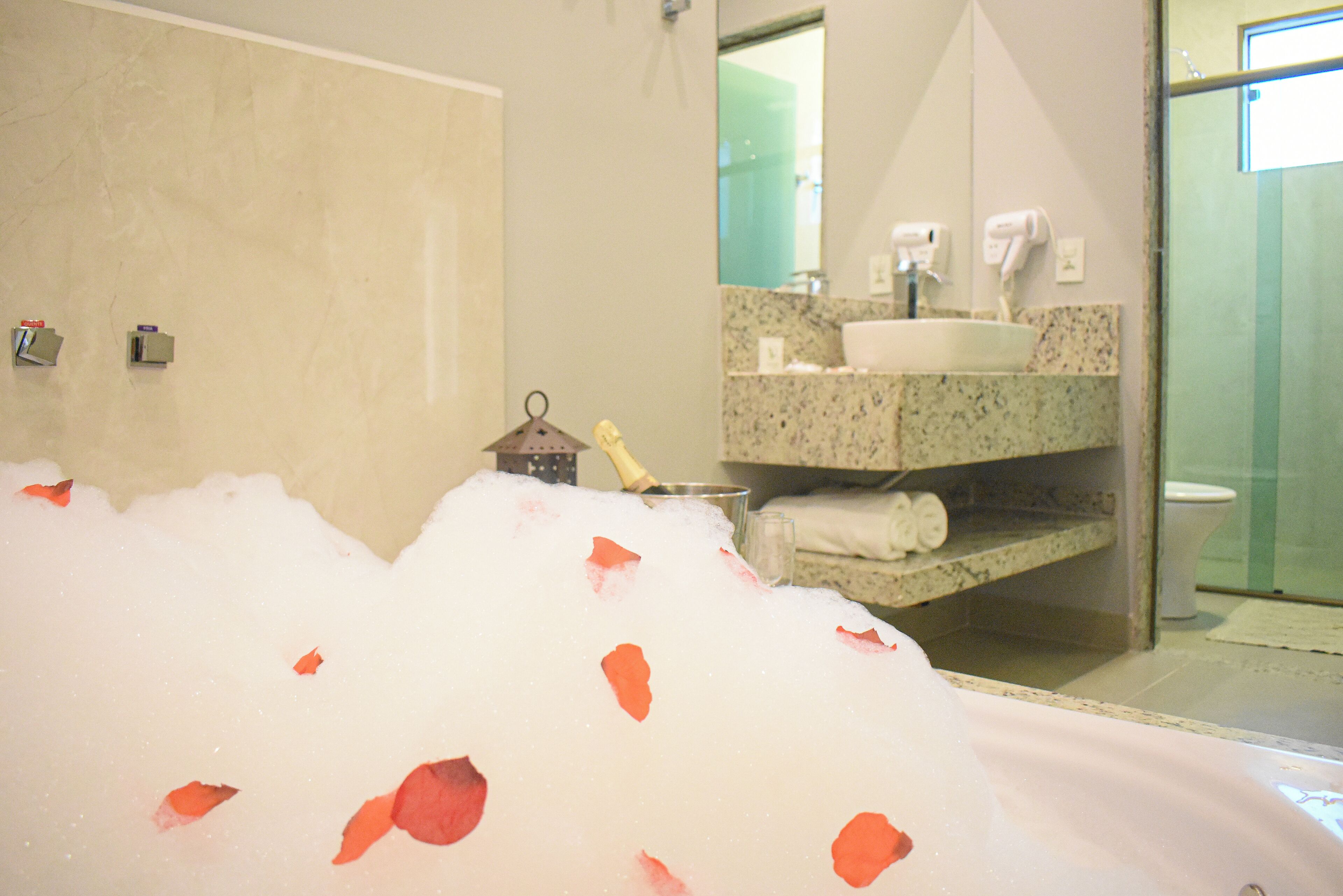 A bathroom with a bathtub filled with bubbles and rose petals, a sink, and a toilet.