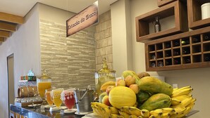 Zona de bufé con diversas frutas, dispensador de jugo y una estantería para vinos.