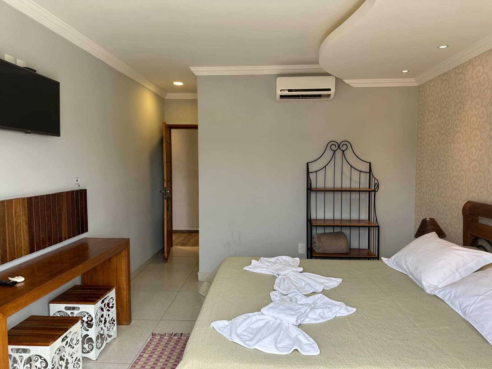 A hotel room with a bed, a bench, a wardrobe, and a television.