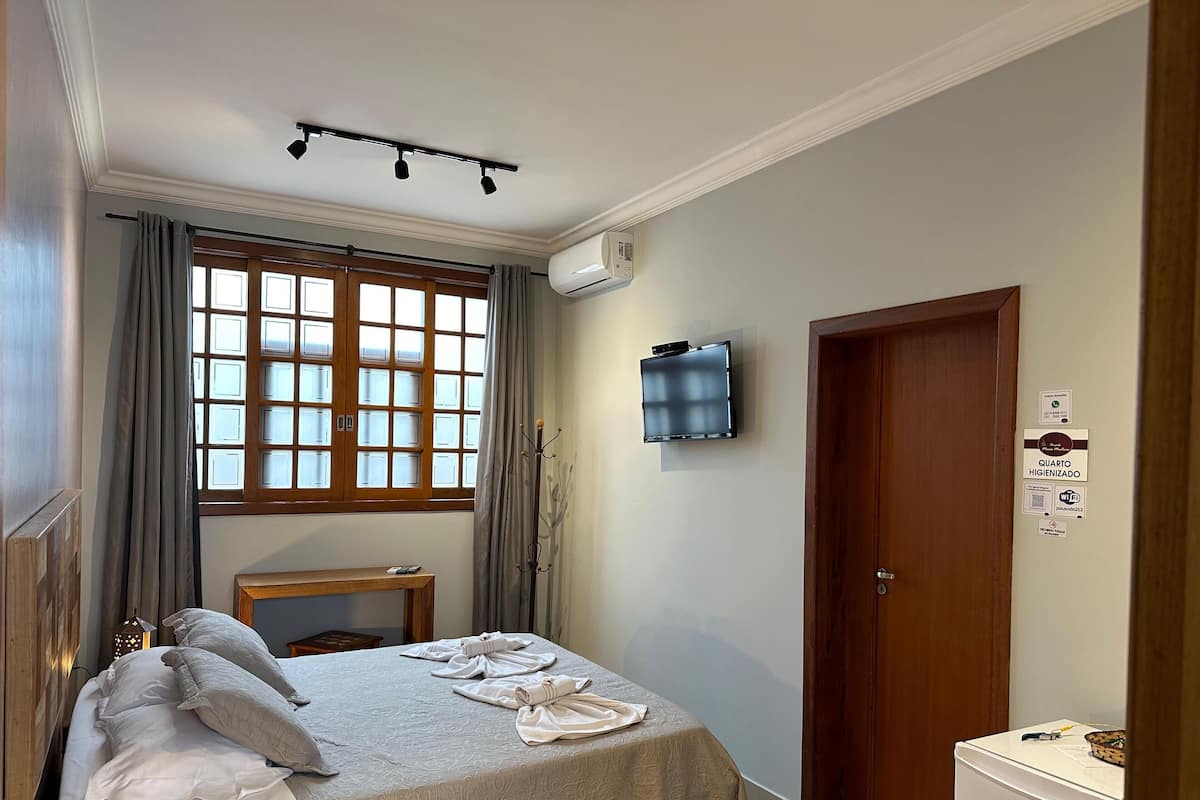 Quarto de hotel com cama, secretária, televisão e porta.