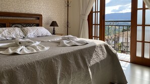 Una cama bien hecha con una colcha estampada, una lámpara de noche y vistas a un balcón con barandilla.