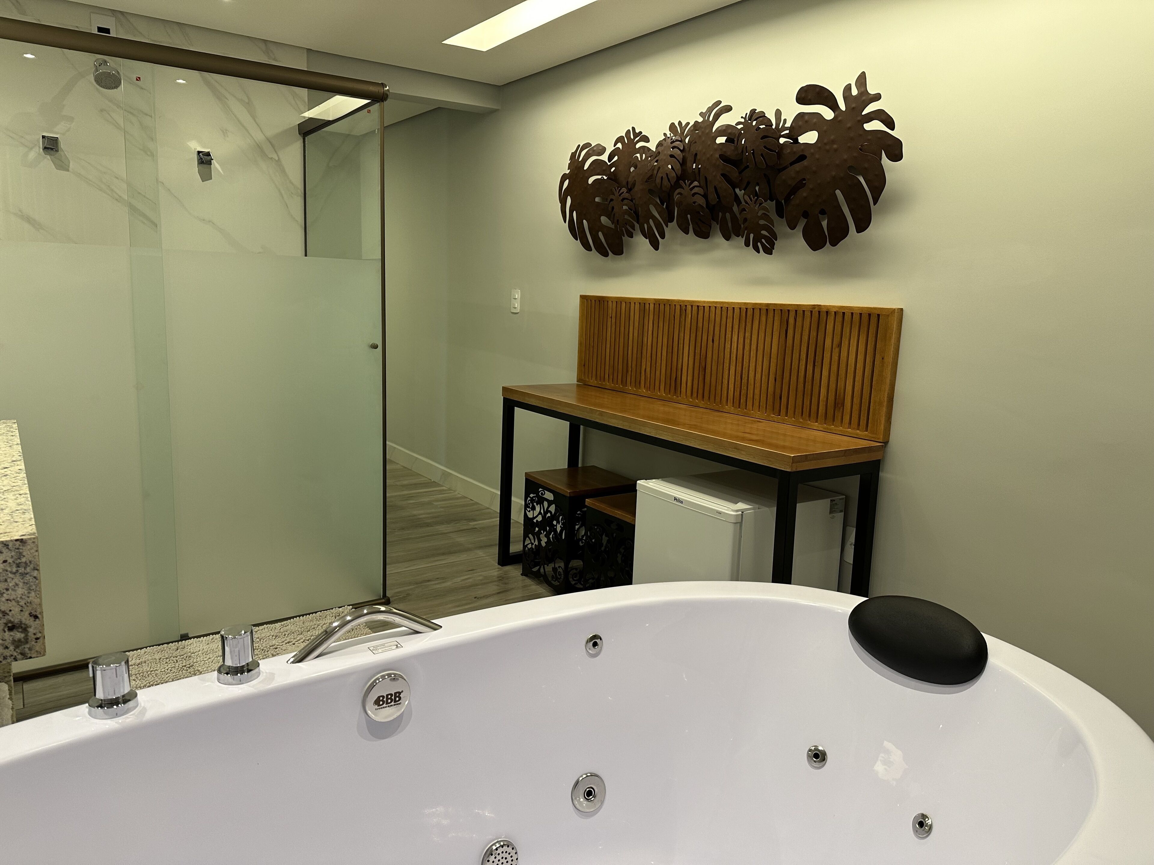 A modern bathroom with a freestanding bathtub, a bench, and a decorative wall piece.