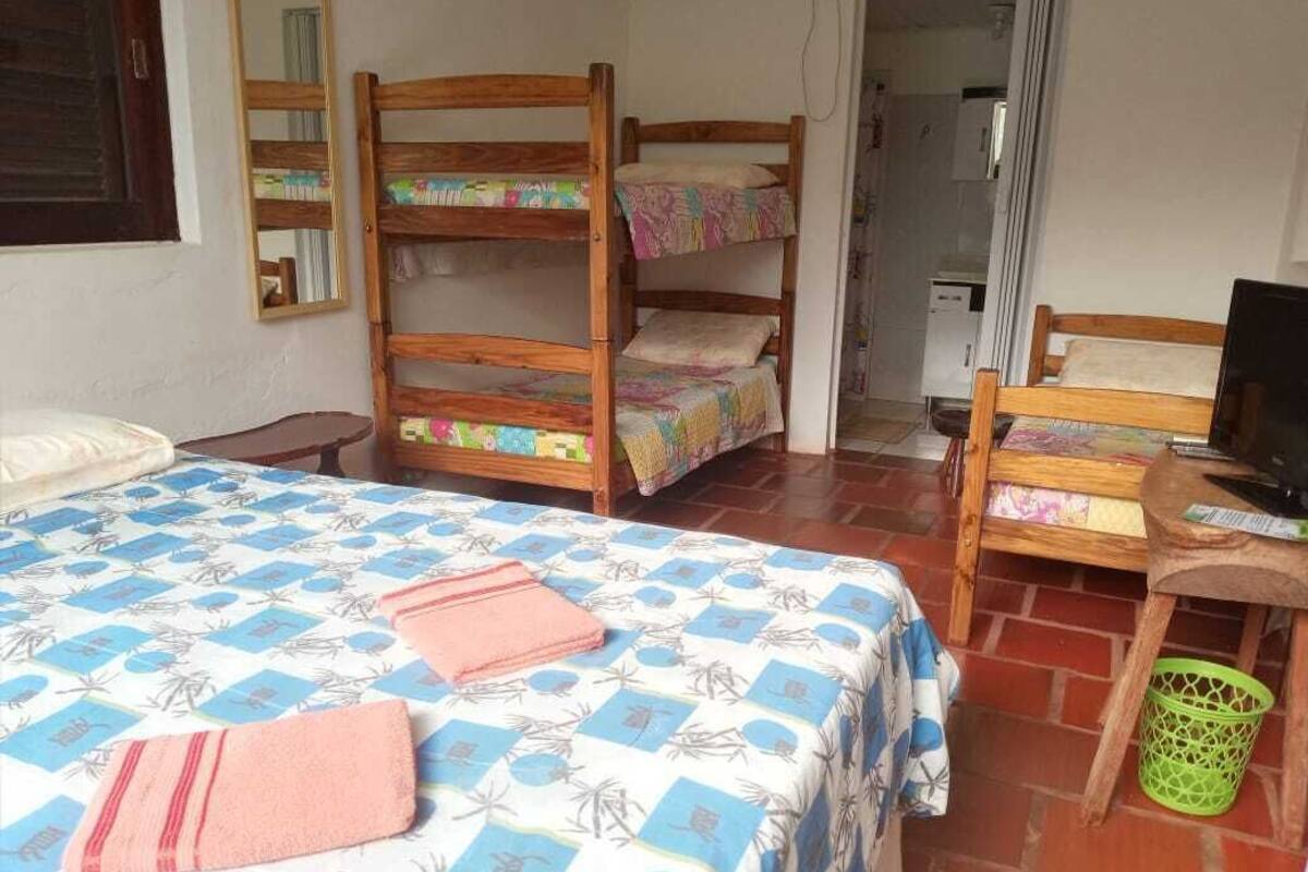 A room with a bed, bunk beds, a desk with a computer, and a green basket.