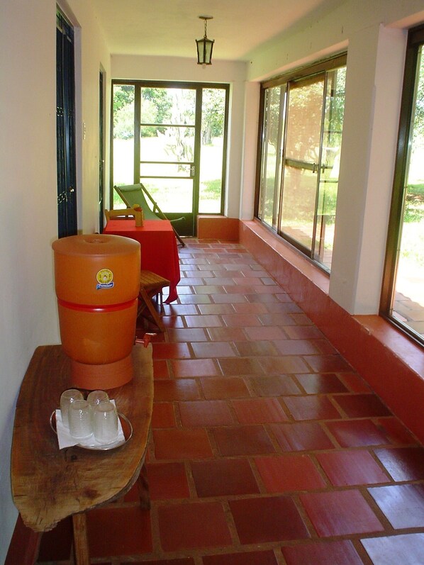 A corridor with a tiled floor, a wooden bench with a water dispenser, and a table with cups. - Sitio Preserva (São Borja)