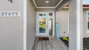A modern entrance with a glass door, a welcome sign, and a number plaque on the wall.