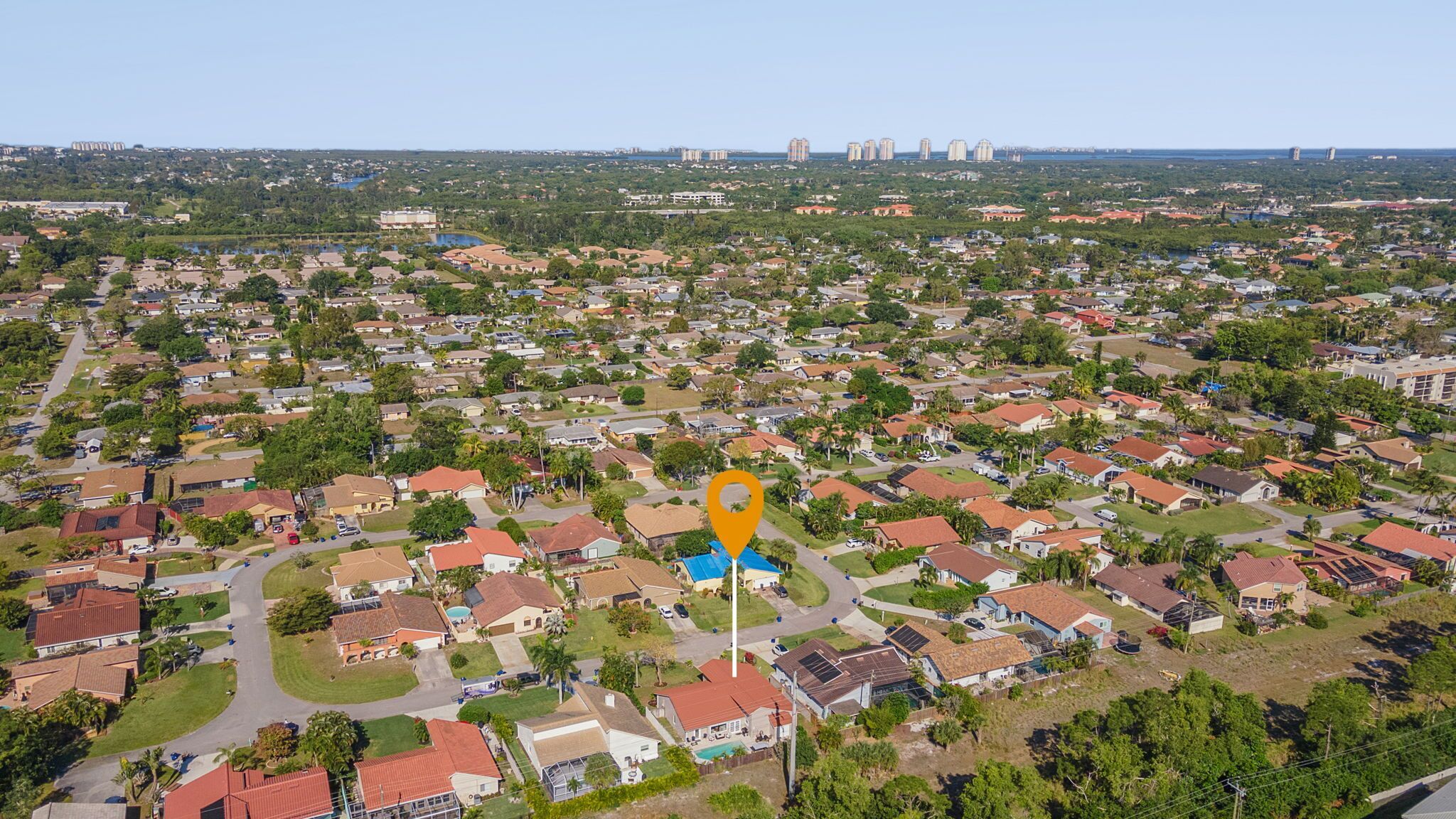 Vista aérea de una zona residencial con casas unifamiliares y edificios de apartamentos, con una calle central y vegetación circundante.
