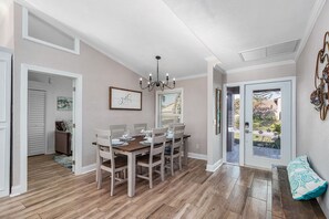 Un coin repas avec une table et des chaises en bois, un lustre et une vue sur une terrasse extérieure, accessible par une porte vitrée.