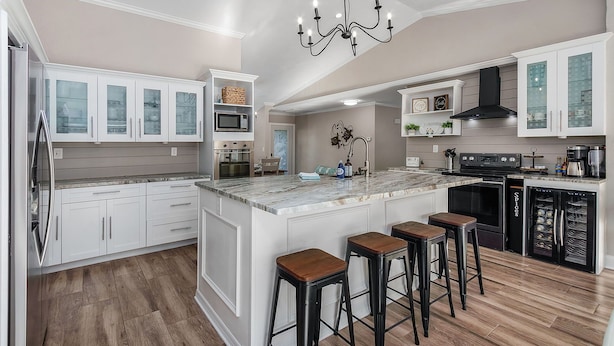 A modern kitchen with white cabinetry, a marble island, and a black range hood.