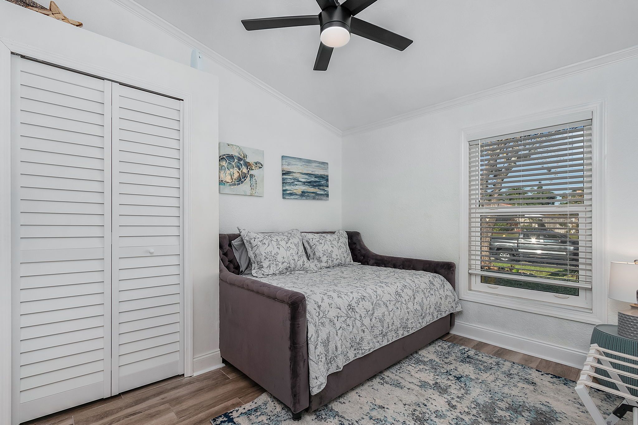 Une chambre à coucher comprenant un lit, un ventilateur de plafond, une fenêtre avec des stores et un placard.