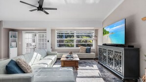 A living room with a sofa, coffee table, TV, and a view of a beach through large windows.