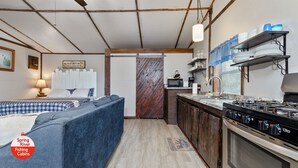 A cozy cabin interior with a bed, sofa, kitchen area, and a wooden door.