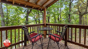 A wooden deck with two folding chairs and a small round table, surrounded by trees.