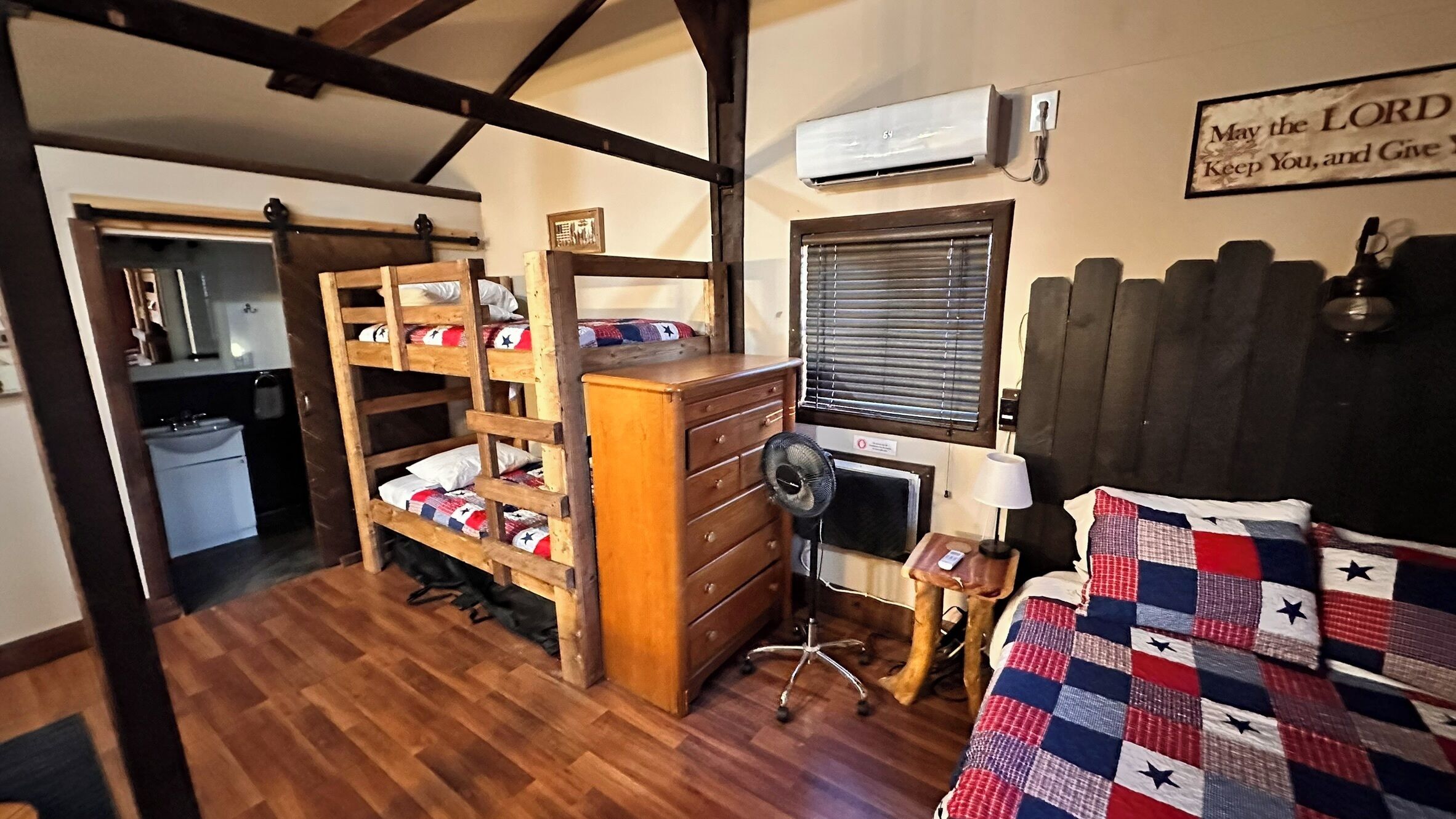 A compact room with a bunk bed, a desk with a chair, a small heater, and a window with blinds.