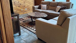 Un salon chaleureux avec un plafond en bois, un canapé beige, une petite table basse et un tapis à motifs.